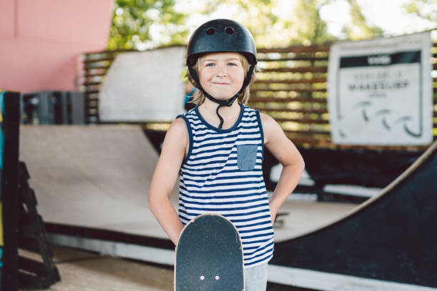 istock children boy with skateboard, weekend breaks, education training, first steps on board. Skateboarder boy. Smiling stylish kid youngster holding skate board outdoors. lad Looking at camera 1253437586