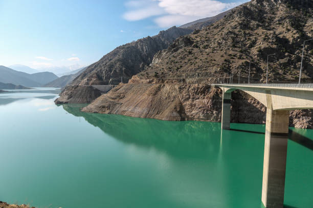 istock Damn bridge by a mountain range with azure water flowing in between 1253439498