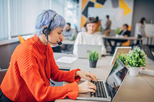 istock Woman using laptop and headset in modern office 1253439686