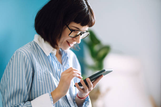 istock Young woman using mobile phone while working at home with laptop. 1253440933