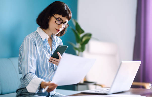 istock Young woman using mobile phone while working at home with laptop. 1253440950
