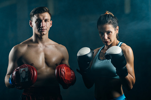 Portrait of serious, young couple with boxing gloves looking at camera in the gym.