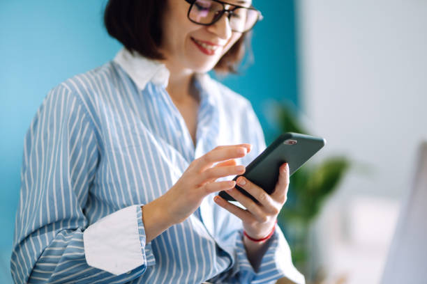 istock Young woman using mobile phone while working at home with laptop. 1253442289