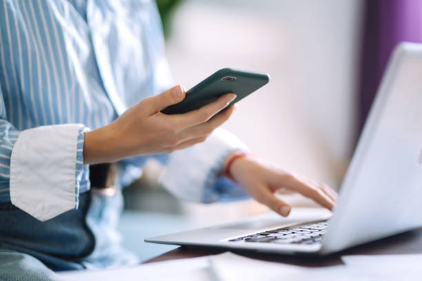 istock Young woman using mobile phone while working at home with laptop. 1253442290