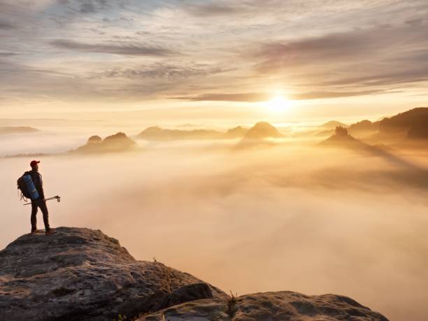 istock Tired Hiker With Sporty Backpack On Rocky Peak And Watching Into Deep Misty Valley Bellow. Sunny Day 1253446003