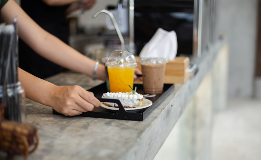 Barista holding tray. selective focus of cake slice with orange juice and ice coffee server for customer