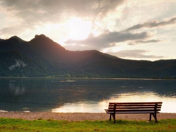 istock Empty Bench At Spring Mountain Lake. The Coast With Mountains At Horizon And In Water Mirror. 1253448269