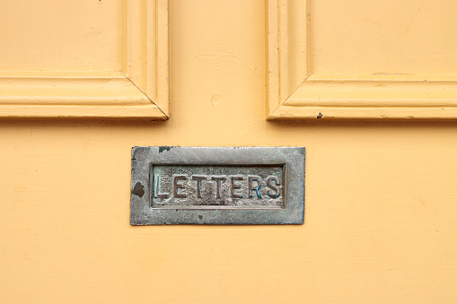 Closeup of an old yellow wooden front door, with brass mail slot.