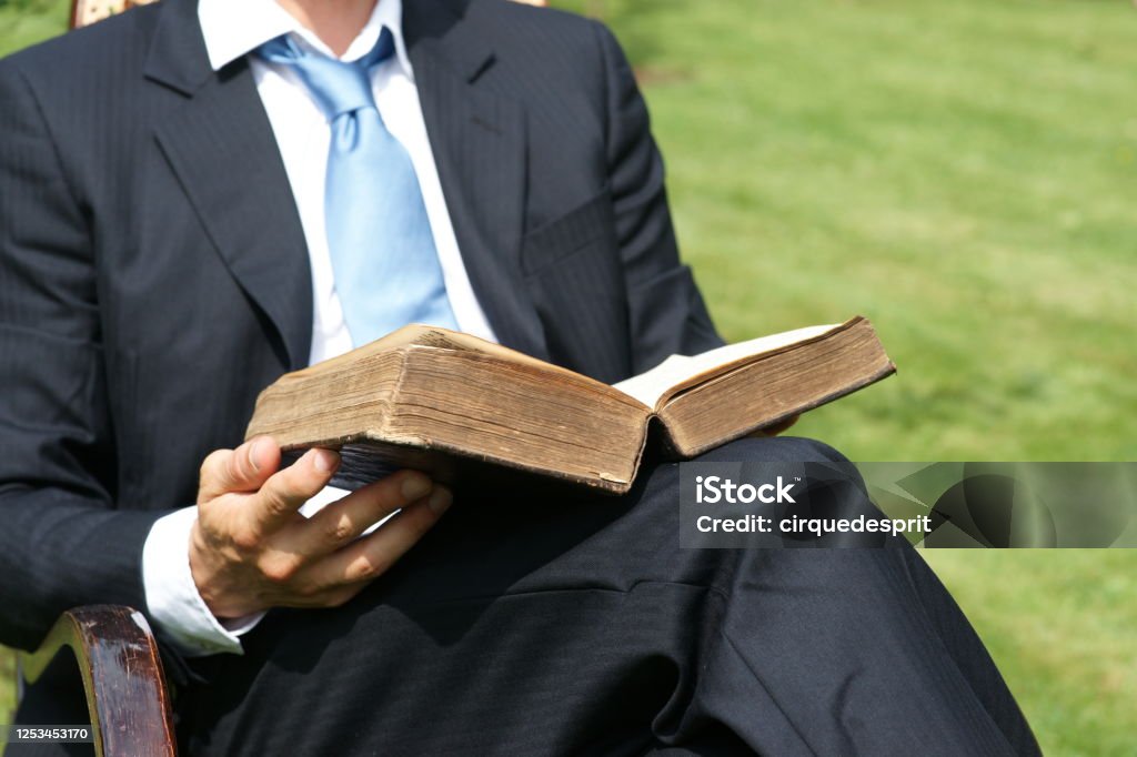 Businessman reading an old book and relaxing in the garden - Close-Up Man sits in chair and reads antique book - bible or law book or dictionary Businessman Stock Photo