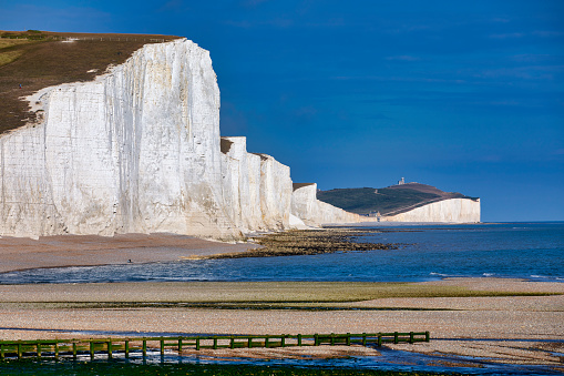 Landscape scene Seven sisters beach and cliffs in southern England. Small lighthouse in the sea with white cliffs and Road