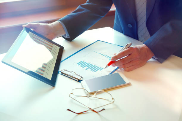 istock Business documents on office table with smart phone and digital tablet and graph financial and man working in the background 1253458725