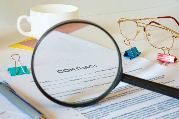 istock Desktop office desk, notebook, glasses, pen and documents. Magnifier approximates the word CONTRACT 1253458743