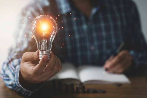 hombre de negocios una mano sosteniendo bombilla con brillo naranja y una idea creativa de escritura a mano en el cuaderno. - authority expertise science and technology technology fotografías e imágenes de stock