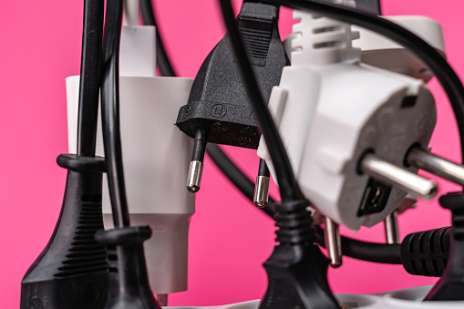 Crowded  white extension cord with many plugs on pink background. The scene is situated in controlled studio environment in front of pink background. Photo is taken with SONY AIII camera
