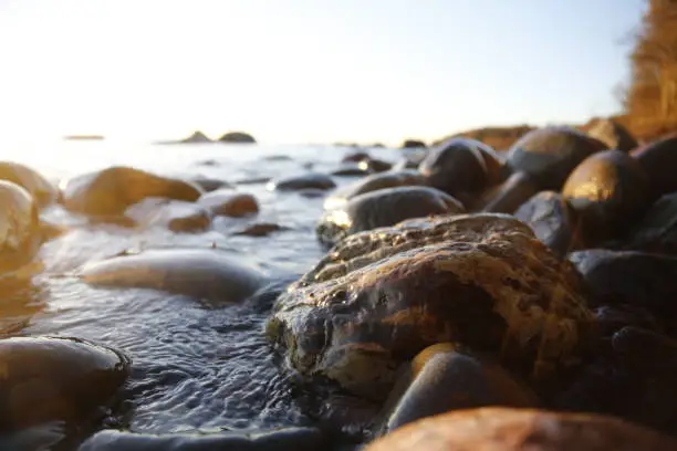 Photo of Closeup photo of sea waves braking on a wet seashore stones summer sunset, water splashes , sun rays, reflections on water drops.