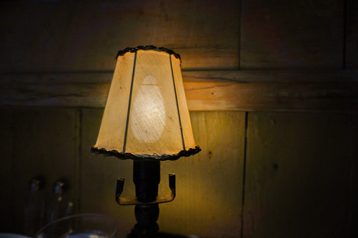 Classic table lamp with turned on bulb under lampshade is on table with cloth.  Authentic fine dining European atmosphere.