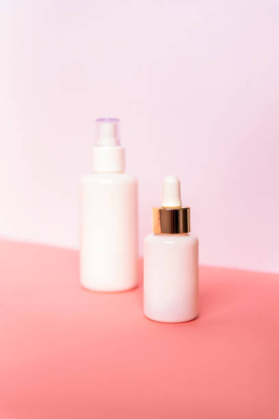 istock Two bottles with serum and cosmetic lotion on pink table against white wall. Unbranded blank packages. Natural skincare 1253463543