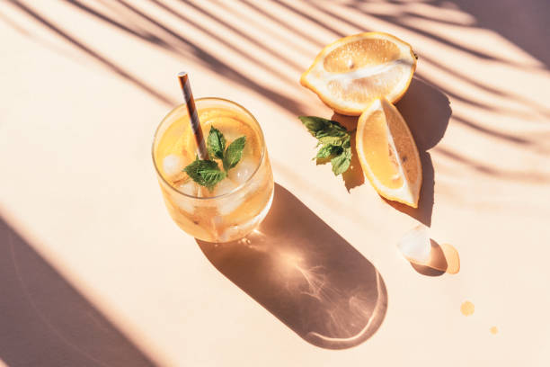 fresh lemonade with mint leaves and ice cubes on yellow background, sharp shadows, top view - chá gelado imagens e fotografias de stock