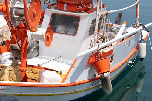 Detail of a fishing boat tied up in a harbor of the Greek Island of Chios in the Aegean Sea. Various fishing gear are lying on or mounted onto the deck of its bow or hanging at the sides of the ship on a sunny day in summer. The fishermen places their nets in the sea at the evening as it gets dark and return to collect the nets with their catch of fish the next morning at sunrise.