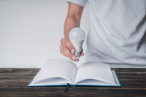 A man holds a light bulb in his hand and puts it on a book, learning concept, innovation concept