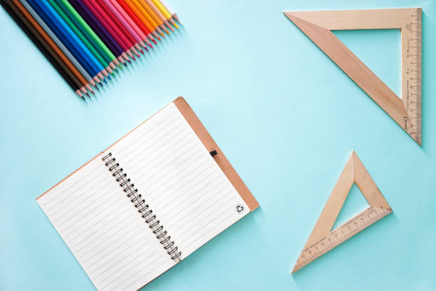Color pencils, two wooden rulers triangles and clear sheet note book on a light blue background. Horizontal photo. Flat lay minimalistic composition. Back to school, college, education concept. Space for text, copy space. Stationery. Art supplies idea. composición plana de primer plano minimalista horizontal con libro de notas de hoja clara, dos triángulos de reglas de madera y lápices de color sobre un fondo azul claro. objetos en el centr y el ángulo superior izquierdo de la foto. papelería. foto