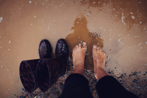 Cropped shot of a woman standing a muddy puddle of water next to her rain boots