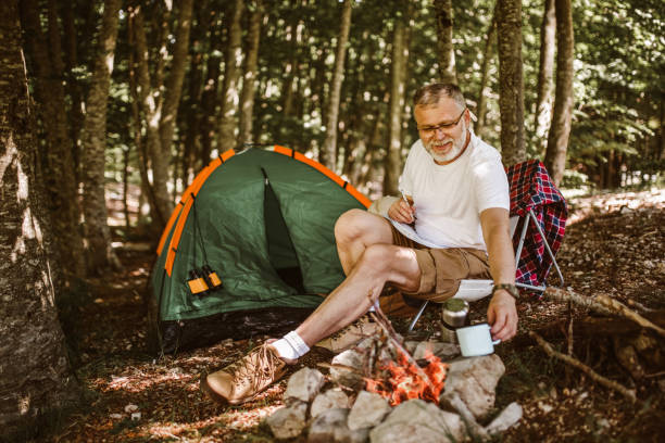 istock Man sitting in front of a tent near campfire 1253464975