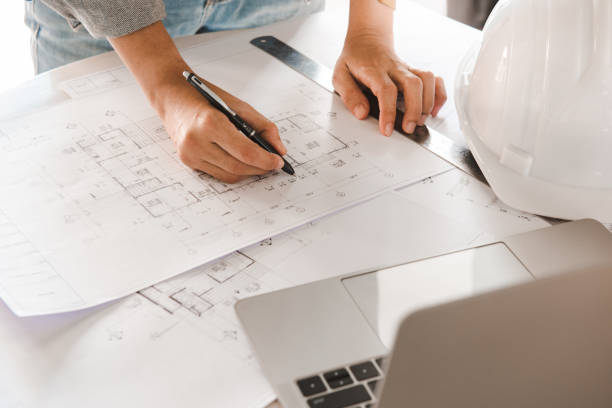 istock Top view of Engineer or architect holding pen with drawings in construction on blueprints in office. Engineering and construction concept. 1253465532