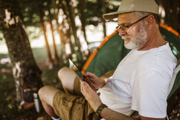 istock Man camping in nature looking at digital tablet and smiling. 1253468375