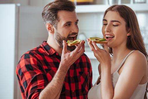 cheerful young couple holding toasts with fresh avocado