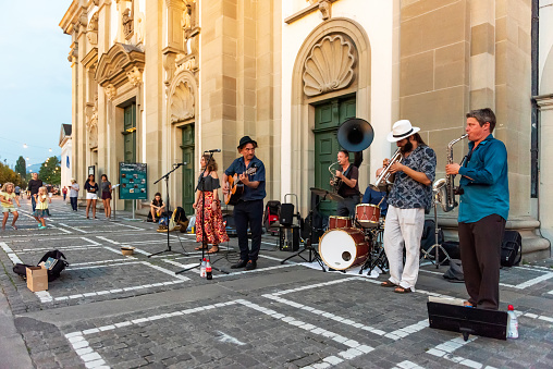 Lucerne, Switzerland - August 21, 2018: The bare brass band busking at Lucerne, Switzerland. Young boys and girls are earning money by using classic musical instruments (trombone, saxophone, oboe, drums, guitar, and soloist) in street of Lucerne. They are street musicians.
