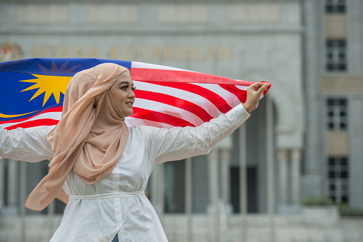 Happy young woman in hijab holding Malaysian flag during Malaysia Day in Putrajaya, Malaysia