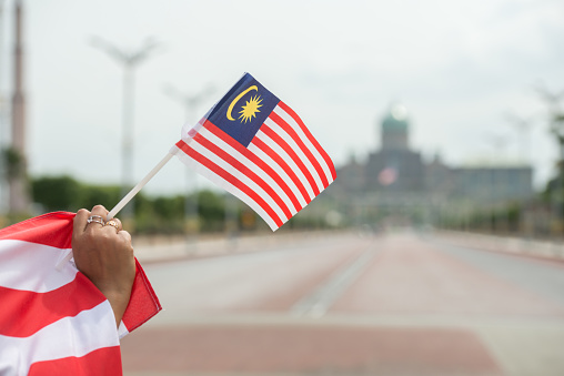 Malay, wearing a traditional shirt, holds the Malaysian flag in front of him