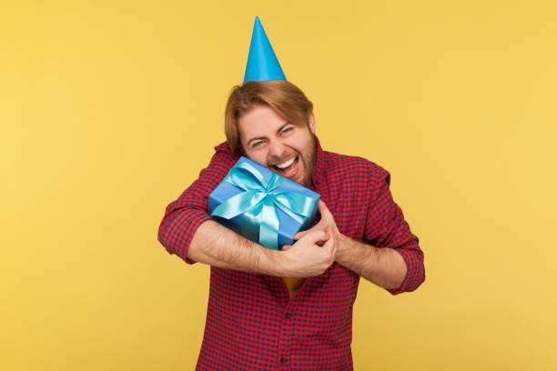 istock Extremely happy guy with funny party cone on head embracing gift box, shouting for joy excitement, indoor 1253479089