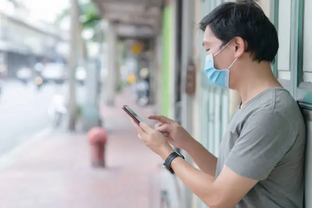 Man on the street with a blue face mask staring at his cell phone