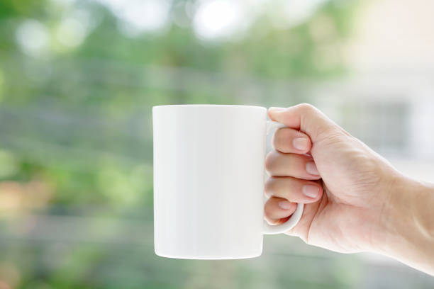 Close-up photos mock up man's hand holds a white coffee mug, nature bokeh background.