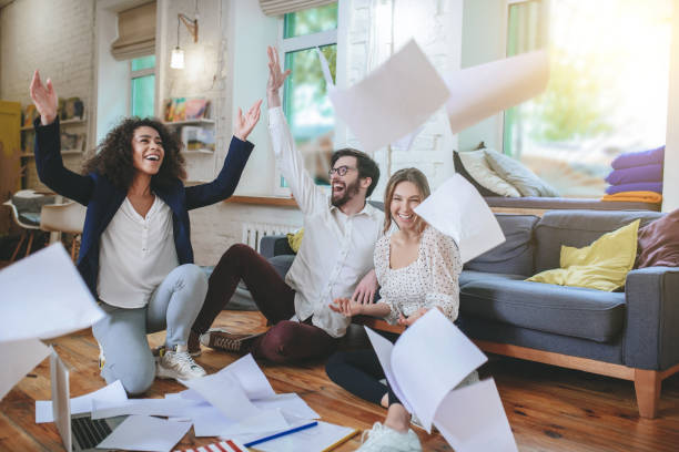 istock Three young friends sitting on floor throwing up documents 1253484594