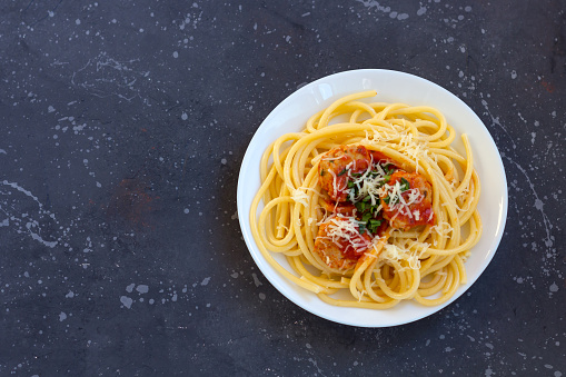 Spaghetti with meatballs, tomato sauce and parmesan cheese in white plate on dark background. Italian pasta concept. Close up, copy space