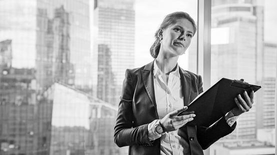 Young woman working at the office. Standing near window with city panorama in background. Black and white photography