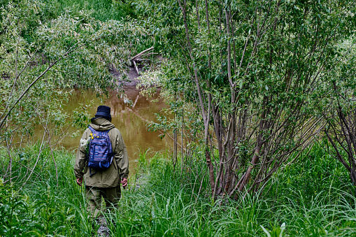 Active man in mosquito suit with backpack in hiking near taiga river in a siberian forest, Russia. Solo traveling, lifestyle, domestic tourism concept