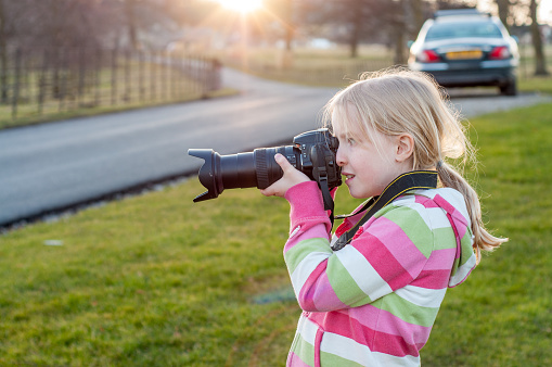 A young blonde girl using a camera with a large zoom lens. Back lit by setting golden sun.