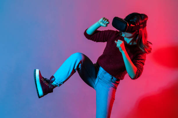istock Leisure activity. Girl with virtual reality glasses playing game simulator, raising leg fighting or passing obstacles 1253489964