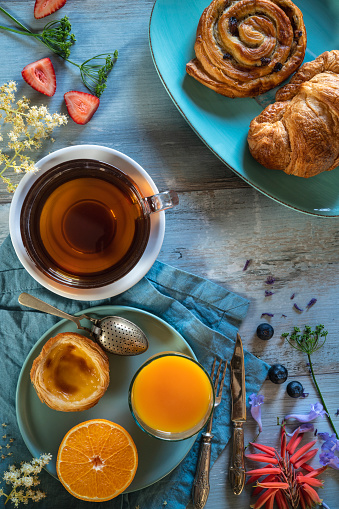Breakfast Tea cup with pastries Cinnamon roll croissant and Portuguese egg tart with orange juice on light blue table with flowers