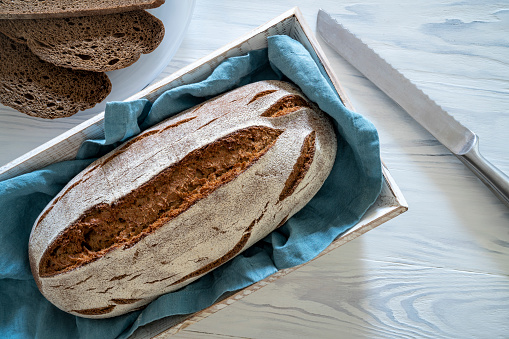 Wholegrain rye bread loaf on white wooden background, bread slices and kitchen knife