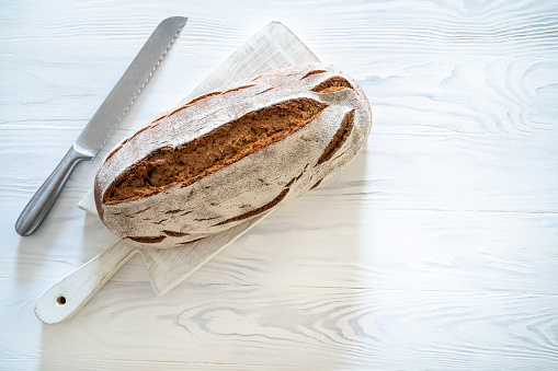 Wholegrain rye bread loaf on white wooden background with break knife