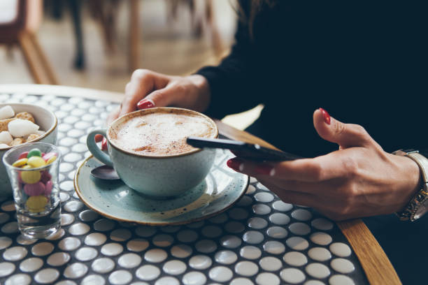 istock Close-up of woman's hands holding cell phone while sitting in modern cafe. 1253493932