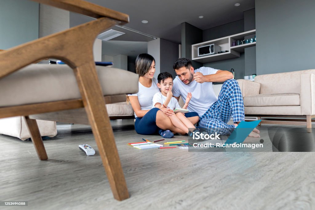 mom, dad and son do homework Mom, 26-year-old Latin woman dressed casually and dad, average Latino man of 30 years, dressed casually, are inside their house with their little 6-year-old son who helps them do their homework on the floor, we observe colors, pencils, paints and notebooks Child Stock Photo