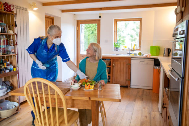 Enjoy Your Food A frontline worker puts down her senior client who is shieldings food and is keeping safe during the coronavirus pandemic by wearing her PPE consisting of mask, gloves, apron making sure to keep a practical distance. meals on wheels photos stock pictures, royalty-free photos & images