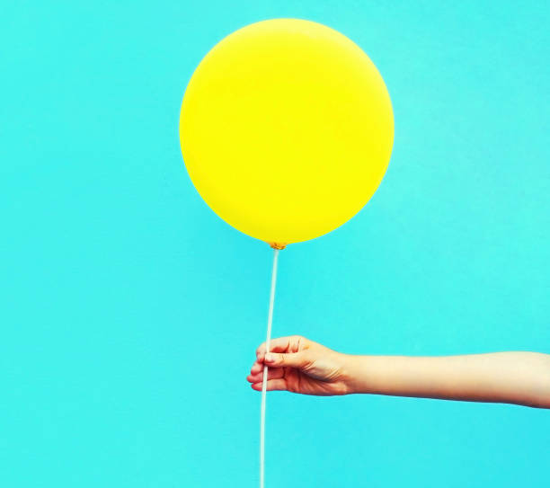 istock Hand holding yellow balloon on colorful blue background 1253501546