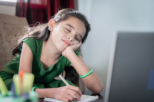 Girl child sleeping during online class in front of laptop - concept of tired kid from distance learning or online education at home during covid-19 or coronavirus lockdown